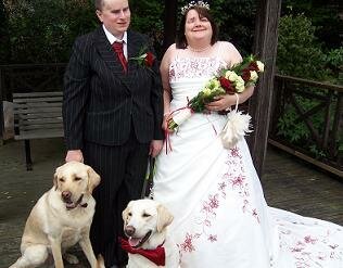 Lee in a smart suit and Jess in a white dress with guide dogs